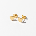 A pair of small gold heart stud earrings with flat polished hearts and butterfly backings, displayed on a clean white background.