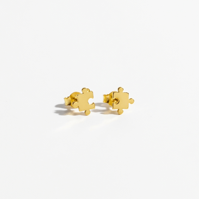 A pair of small gold stud earrings shaped like interlocking puzzle pieces, photographed on a clean white background.